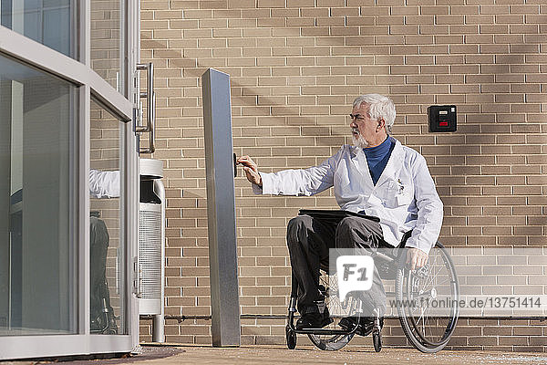 Doctor with muscular dystrophy in wheelchair at hospital entrance pressing knob for accessible door