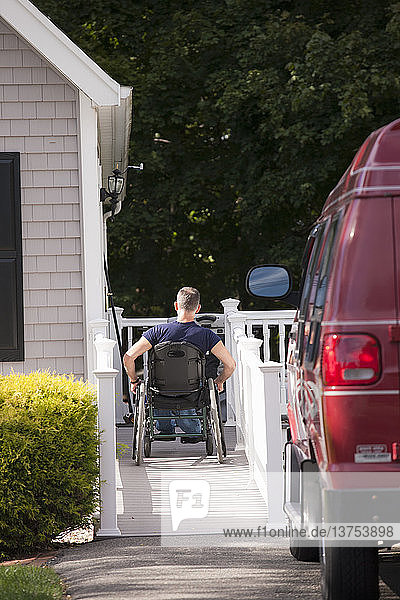 Mann mit Rückenmarksverletzung im Rollstuhl fährt die Rampe seines Hauses hinauf