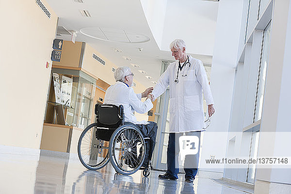 Arzt mit Muskeldystrophie im Rollstuhl schüttelt einem anderen Arzt die Hand