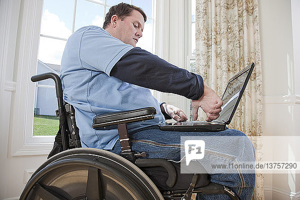 Mann mit Rückenmarksverletzung im Rollstuhl arbeitet mit seinen behinderten Händen an einem Laptop