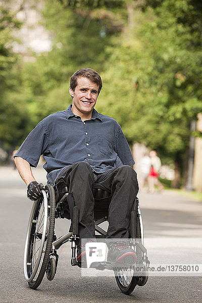 Man with spinal cord injury in a wheelchair maneuvering wheelchair on path through public park