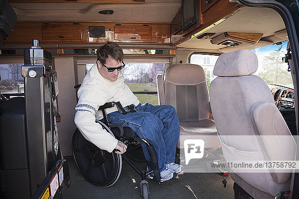 Ein Mann mit einer Rückenmarksverletzung steigt aus seinem Rollstuhl in den Fahrersitz eines behindertengerechten Lieferwagens