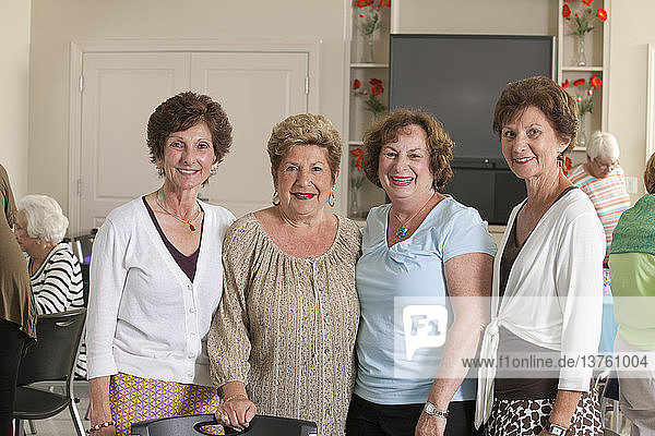 Porträt von vier älteren Freundinnen  die bei einem Mittagessen lächeln