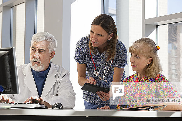 Two nurses and a doctor working on computer and tablet