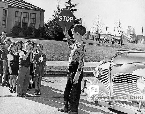 United States: c. 1948 A school crossing guard holds his sign high so that the younger children will not cross the street until he has given them the walk sign.