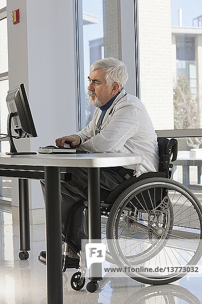 Doctor with muscular dystrophy in wheelchair studying information on his computer