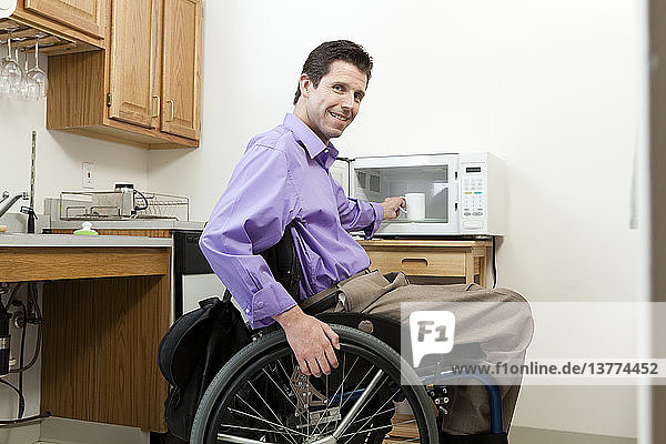Mann im Rollstuhl mit Rückenmarksverletzung entnimmt Tasse aus einer zugänglichen Mikrowelle