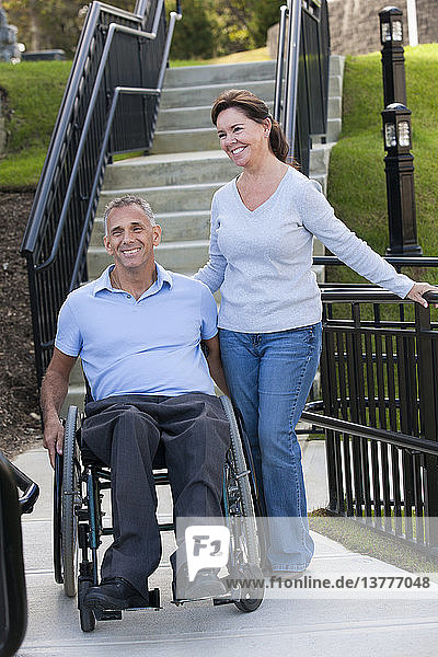 Frau mit Ehemann im Rollstuhl mit Rückenmarksverletzung auf zugänglicher Rampe stehend
