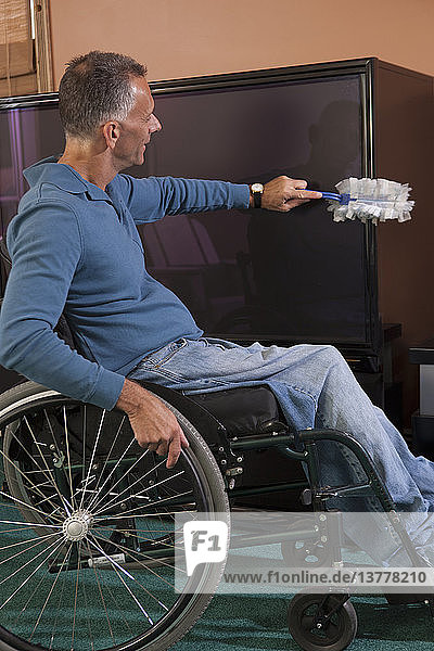 Mann mit Querschnittslähmung im Rollstuhl beim Abstauben von Möbeln