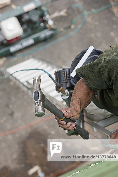 Hispanischer Zimmermann klettert mit Hammer und Nagelpistole auf eine Leiter in einem im Bau befindlichen Haus