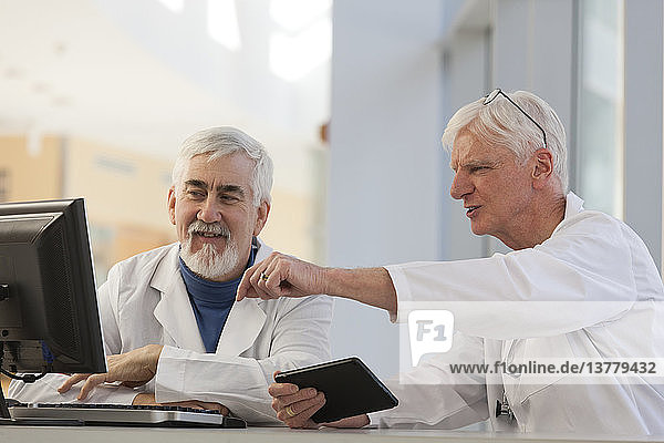 Two doctors discussing information on a computer and a tablet