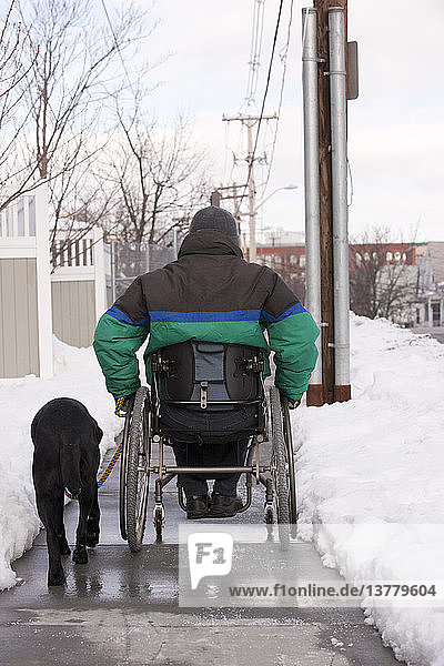 Frau mit Multipler Sklerose im Rollstuhl mit einem Diensthund auf einer verschneiten Straße