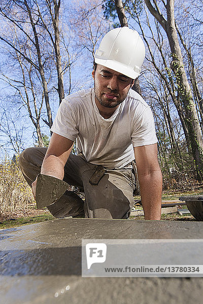 Hispanic carpenter using trowel to smooth concrete for staircase footing