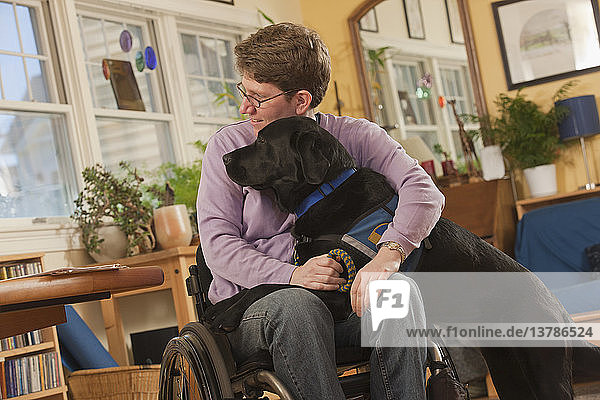 Frau mit Multipler Sklerose im Rollstuhl umarmt ihren Diensthund