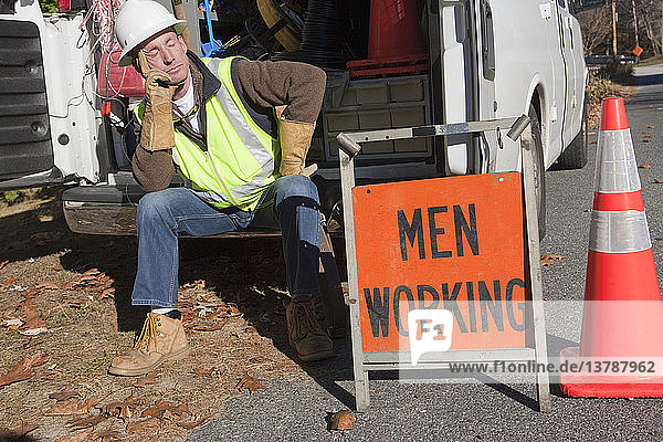 Ein Kabelinstallateur sitzt in einem Lkw in der Nähe eines Men at Work-Schildes