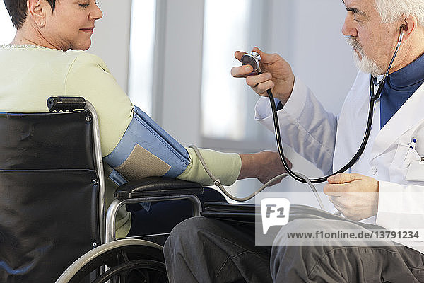 Doctor with muscular dystrophy in wheelchair checking the blood pressure of a patient