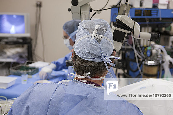 Doctor looking in microscope during surgery with surgical technician taking next instrument