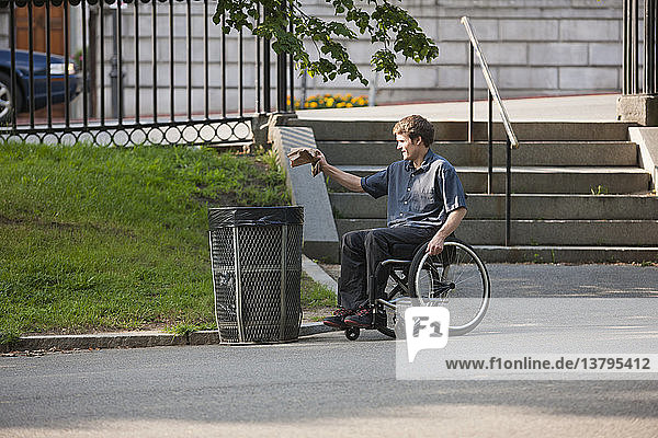 Ein Mann mit einer Rückenmarksverletzung im Rollstuhl wirft in einem öffentlichen Park Müll in einen Behälter