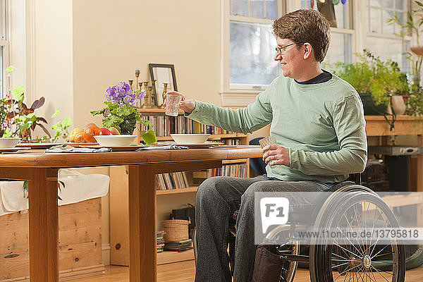 Frau mit Multipler Sklerose im Rollstuhl deckt den Tisch für das Abendessen