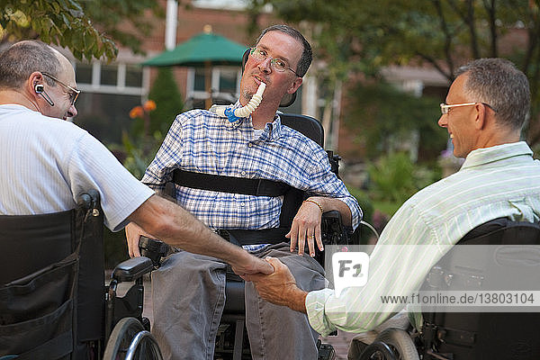 Three men in wheelchairs greeting each other