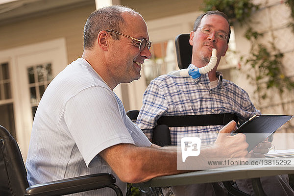 Businessman with Duchenne muscular dystrophy and a man with Friedreich´s Ataxia working at a cafe