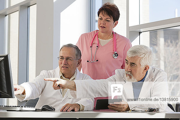 Two doctors and a nurse discussing on a computer and a tablet