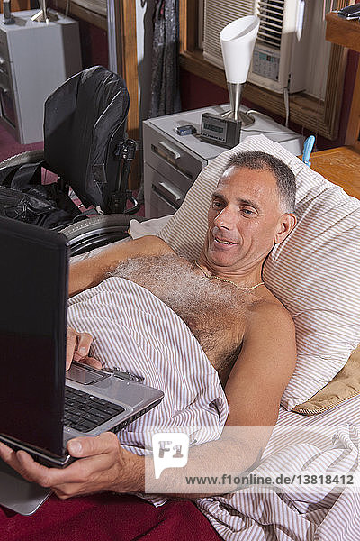 Mann mit Querschnittslähmung im Bett mit seinem Laptop