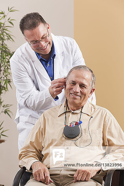 Audiologe passt Hinter-dem-Ohr-Hörgerät im Ohr eines Patienten während der Programmierung an