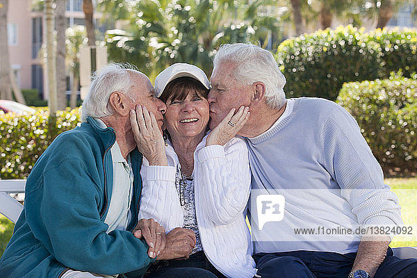 Two senior men kissing their female friend in a park