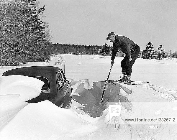 Lansing  Michigan: ca. 1938 Ein Mann in Schneeschuhen blickt auf sein in einer Schneewehe verschüttetes Auto hinunter.