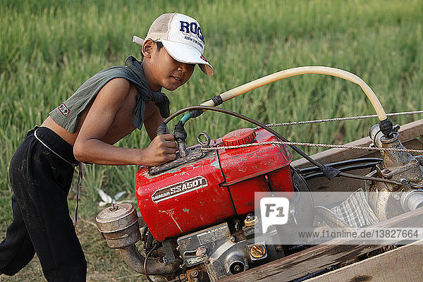 Kambodschanischer Junge  der eine Motorpumpe schiebt