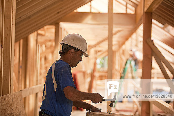 Hispanischer Zimmermann hämmert Nägel auf ein Brett in einem im Bau befindlichen Haus