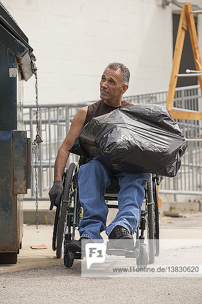 Loading dock worker with spinal cord injury in a wheelchair putting a bag in the dumpster