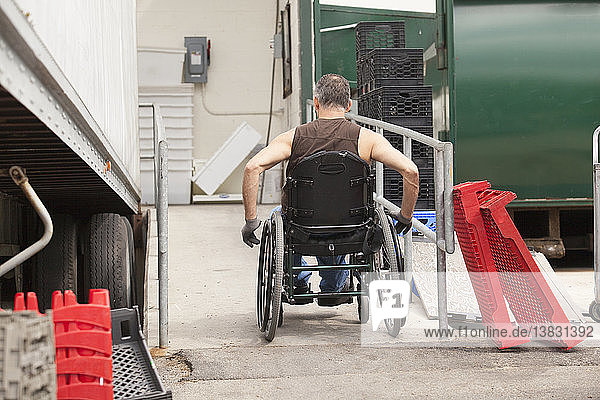 Laderampenarbeiter mit Rückenmarksverletzung im Rollstuhl fährt neben einem Lkw die Rampe hinauf