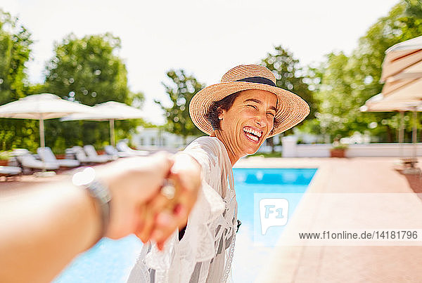 Glückliche Frau führt ihren Mann an der Hand am Pool eines sonnigen Resorts