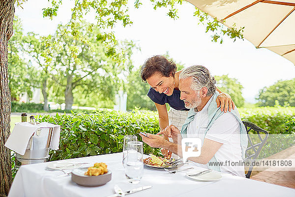 Älteres Paar beim Essen  das am Terrassentisch sein Smartphone benutzt