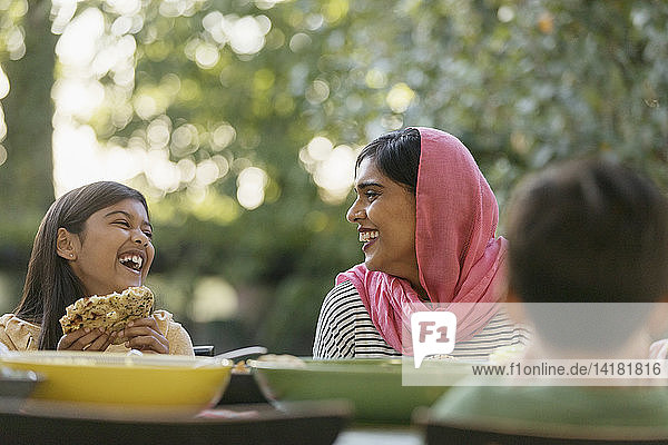 Mother in hijab and daughter laughing at dinner table