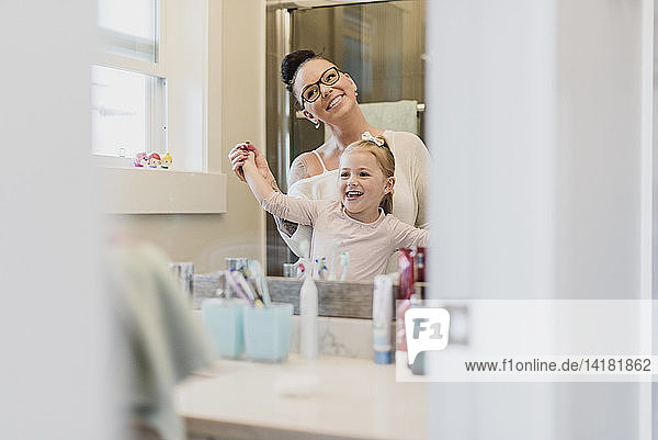 Lächelnde Mutter und Tochter im Badezimmerspiegel