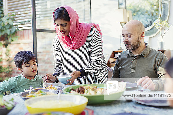 Mother in hijab serving dinner to family at table