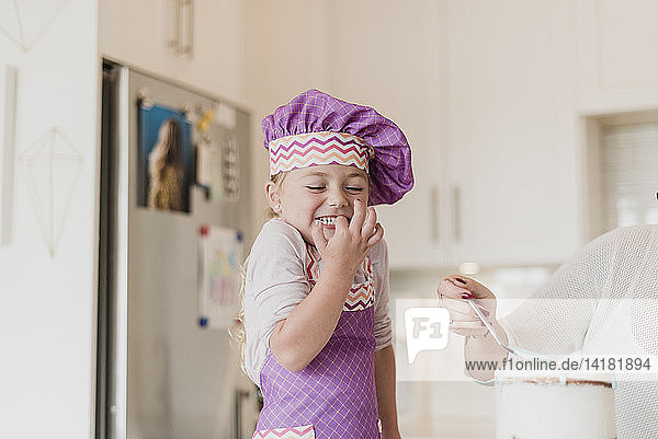 Glückliches  süßes Mädchen mit Kochmütze beim Backen in der Küche
