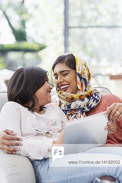 Glückliche Mutter im Hidschab  die mit ihrer Tochter ein digitales Tablet benutzt