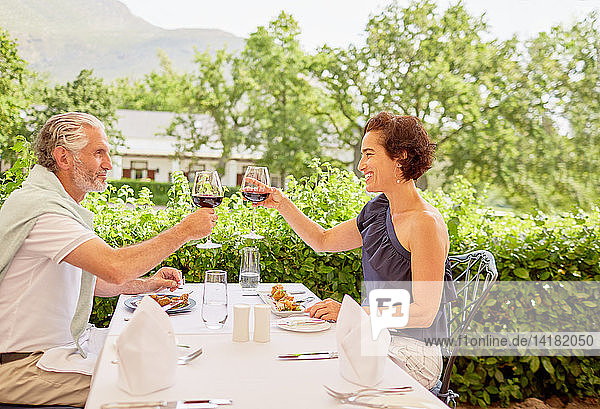 Reifes Paar stößt mit Weingläsern am Tisch eines Terrassenrestaurants an
