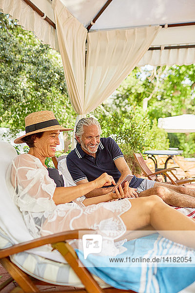 Älteres Paar benutzt Smartphone in Cabana am Pool des Resorts