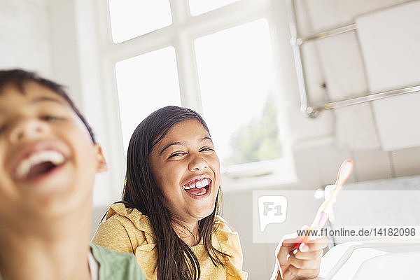 Portrait lachender Bruder und Schwester beim Zähneputzen im Badezimmer