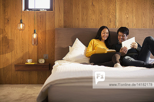 Couple reading book and using digital tablet in bed