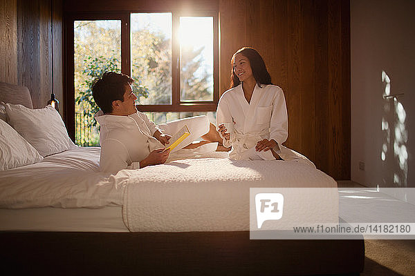Paar in Bademänteln entspannt auf einem Hotelbett