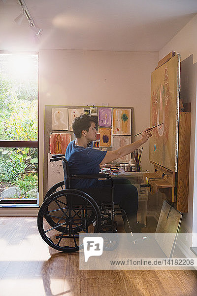 Männlicher Künstler im Rollstuhl malt im Kunstatelier