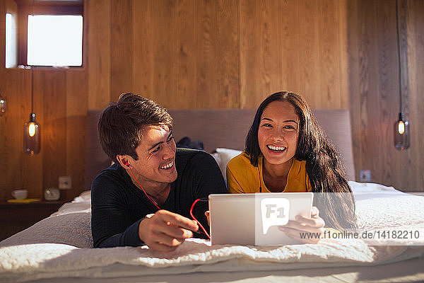 Porträt eines glücklichen Paares mit Kopfhörern und gemeinsamem Laptop auf dem Bett