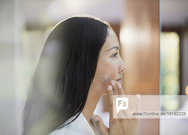 Profile young woman applying moisturizer to cheek