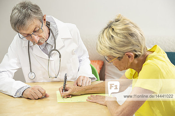 Arzt bei der schriftlichen Rehabilitation einer an Parkinson erkrankten Frau.
